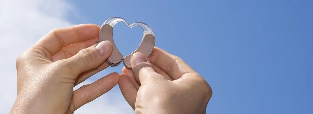 Hands holding hearing aid shells up to the sky to form a heart